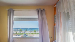 A hotel room with a bed, a window with curtains, a view of the beach and parking area, and a small table with a cup. - Breezot Yam (Nahariya)