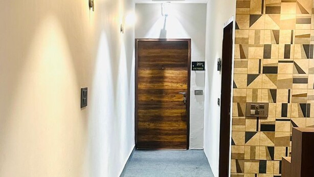 A modern hallway with a wooden door, recessed ceiling lights, and a geometric-patterned wall. - Hotel Primrose - Patiala (Pantran)
