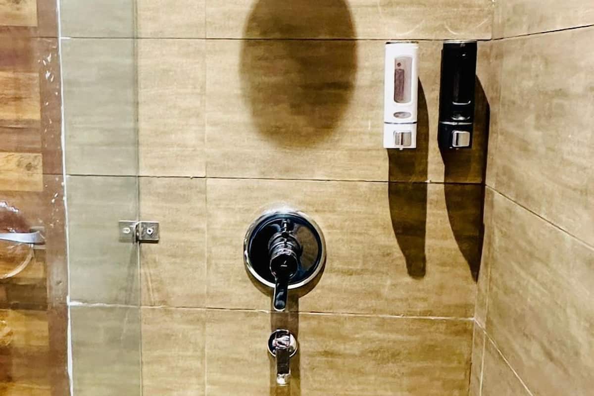 A shower with a handheld showerhead, a control panel, and a wall-mounted faucet.