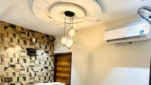 A reception area with a modern design, including a geometric patterned wall, a reception desk, a brown leather sofa, and a ceiling with recessed lighting and a fan. - Hotel Primrose - Patiala (Pantran)