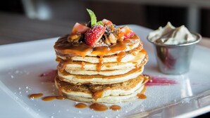 Une pile de crêpes nappées de sauce au caramel et garnies de fruits, le tout présenté sur une assiette blanche.