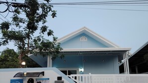 Un edificio con facciata blu, una recinzione bianca e un cartello che indica una stazione di ricarica per veicoli elettrici.