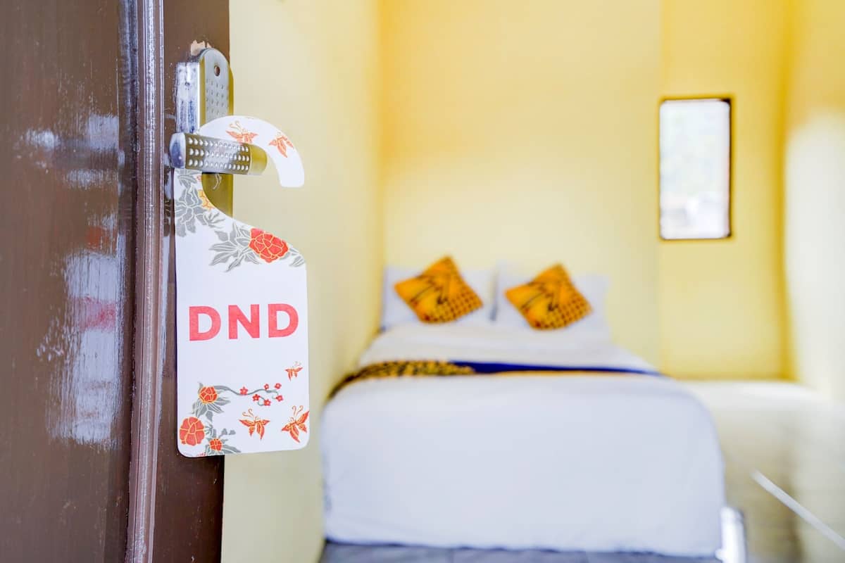 A hotel room with a bed, a door with a DND sign, and a wall-mounted light fixture.