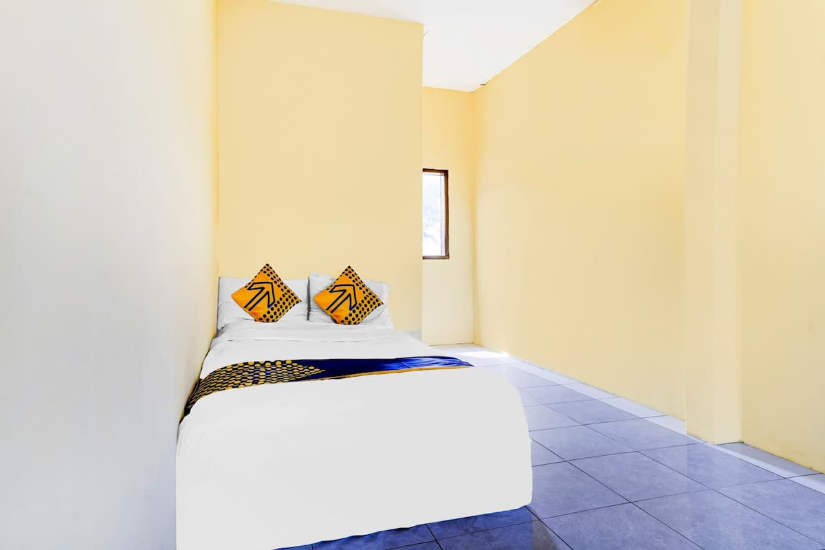 A hotel room with a bed, two pillows with a geometric pattern, a framed picture on the wall, and a tiled floor.