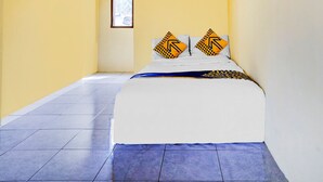 Habitación de hotel estrecha con cama, dos almohadas con flechas direccionales y una ventana en la pared izquierda.