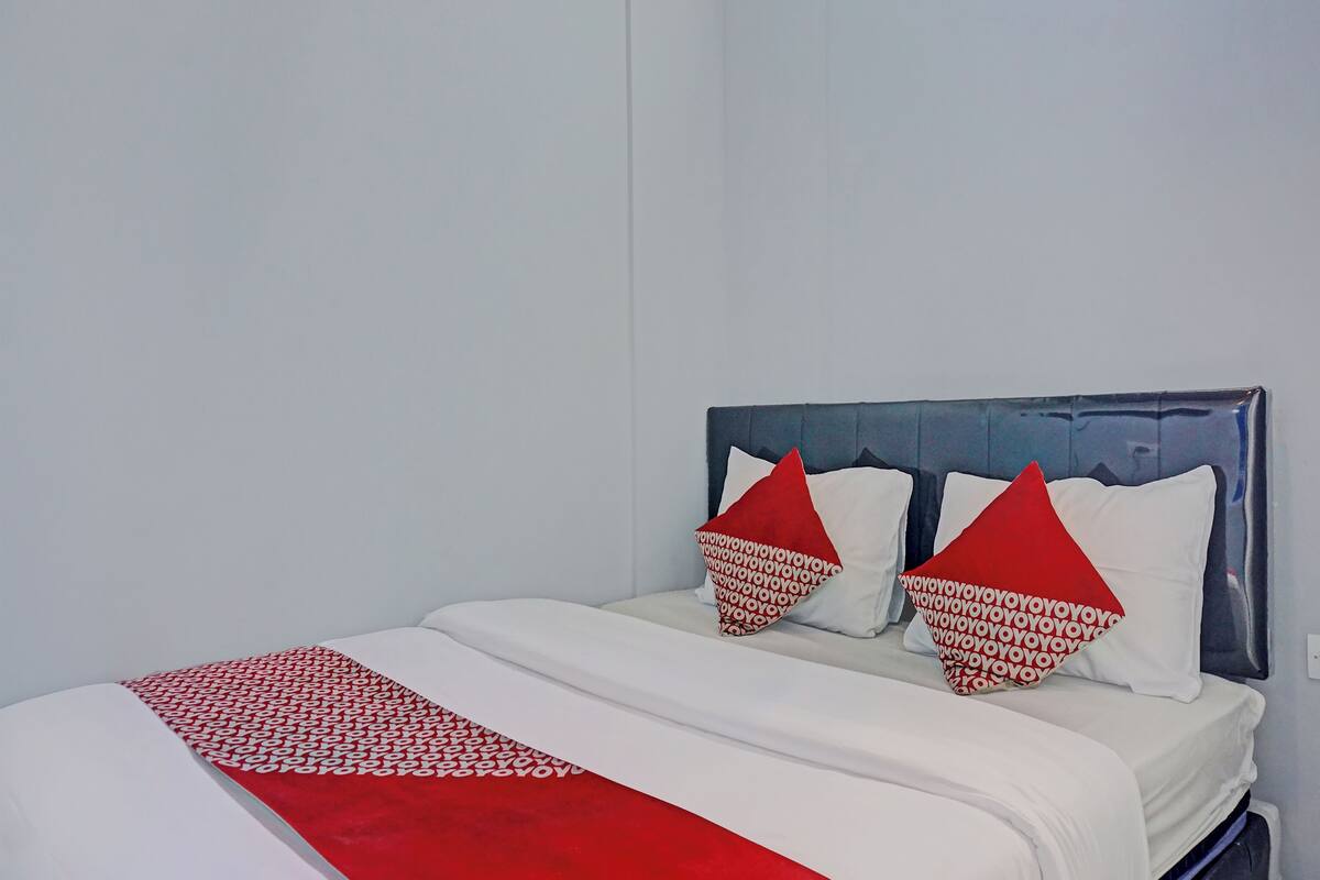 A bed with a white and red bedspread, two red pillows, and a grey headboard.