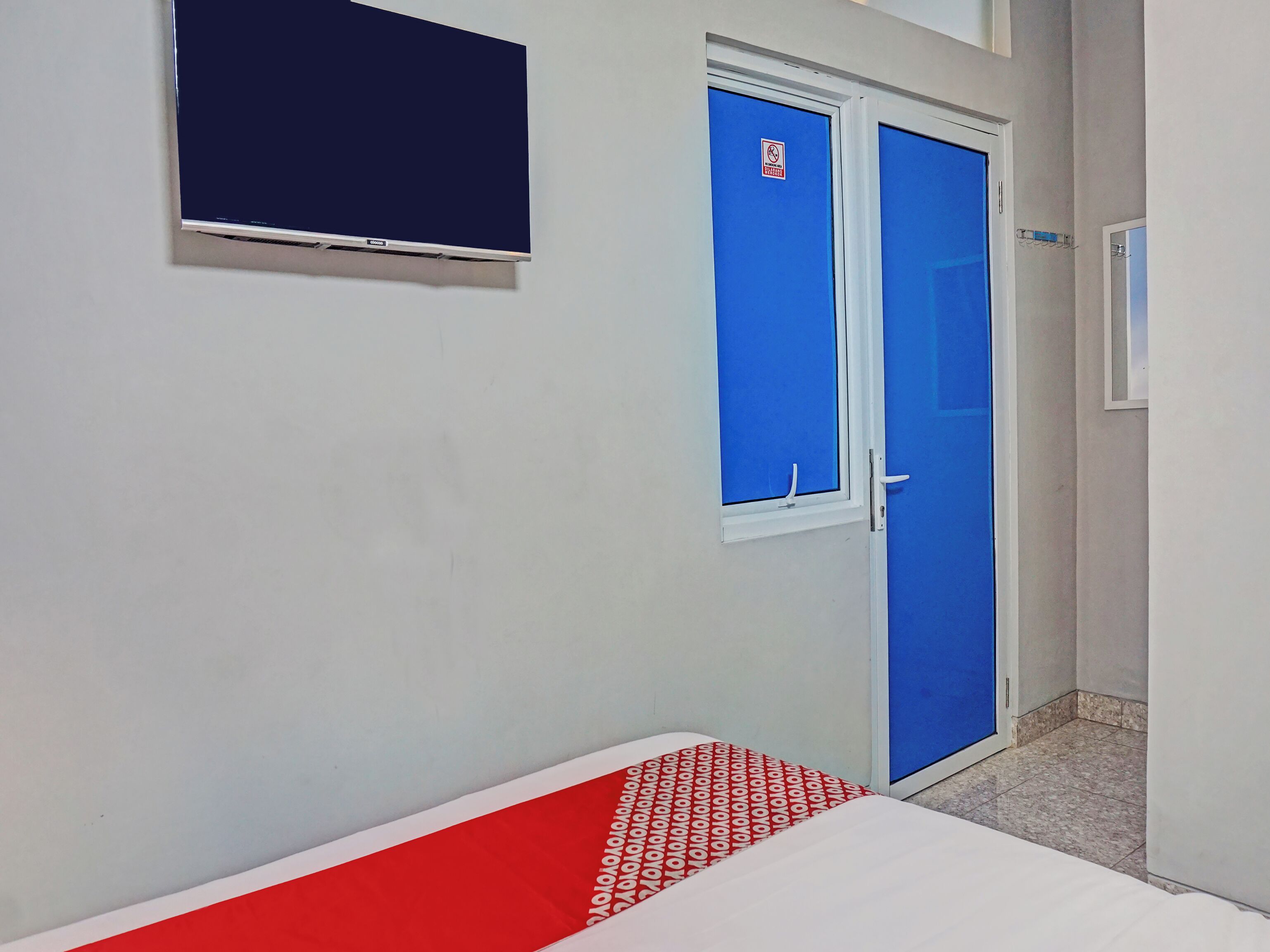 A room with a bed, a TV mounted on the wall, and a blue door with a window.