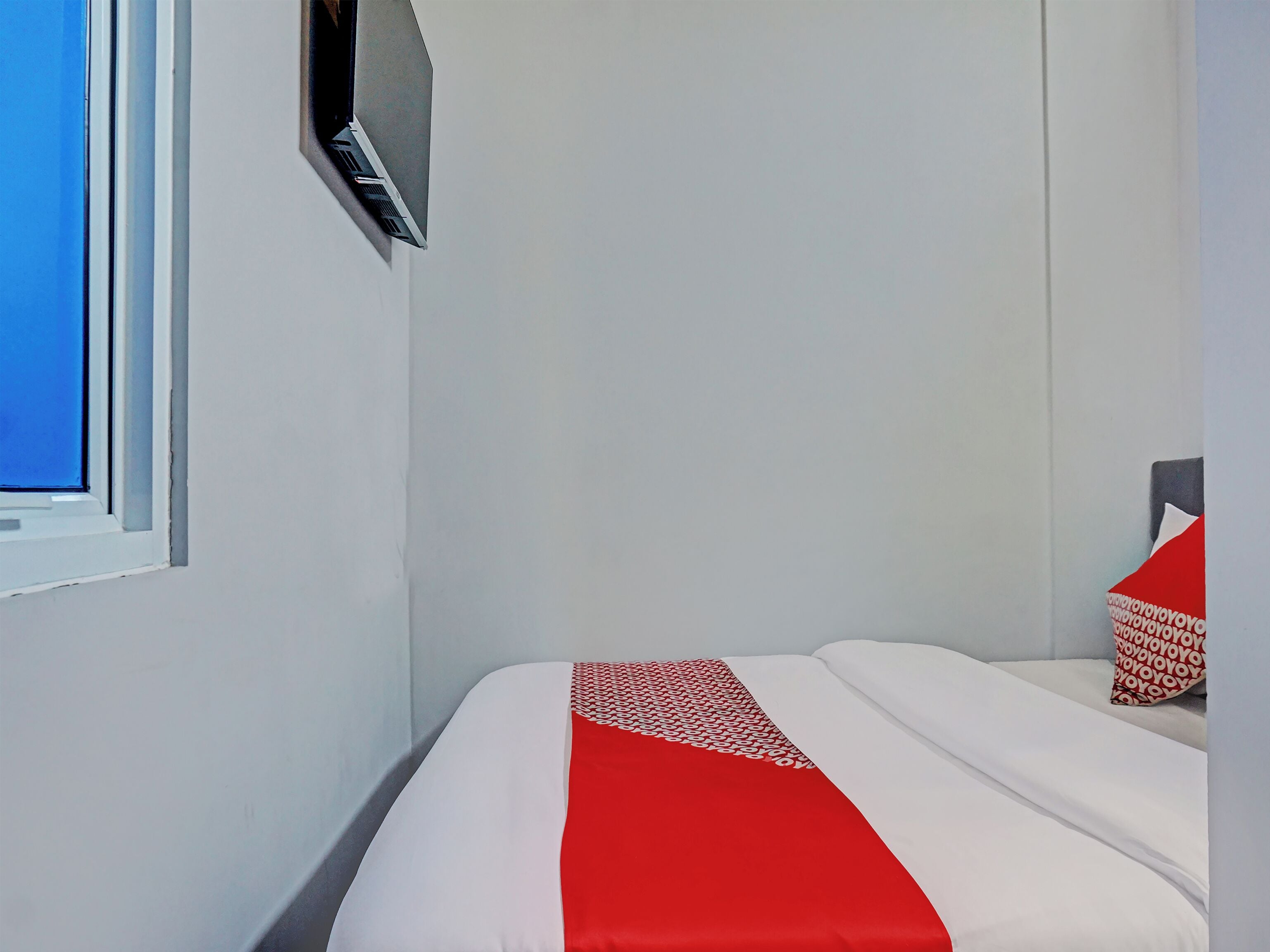 A hotel room with a bed, a TV mounted on the wall, and a window.