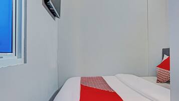 A hotel room with a bed, a TV mounted on the wall, and a window.