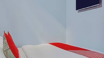 Un dormitorio con cama, almohadas, un televisor montado en la pared y una colcha de diseño rojo y blanco.