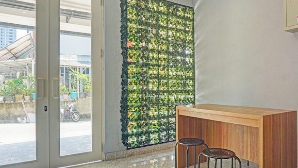 A room with a wooden desk, two stools, a glass door leading outside, and a wall with a green leafy pattern. - Capital O 92765 J&b Smart Sentul (Citaringgul)