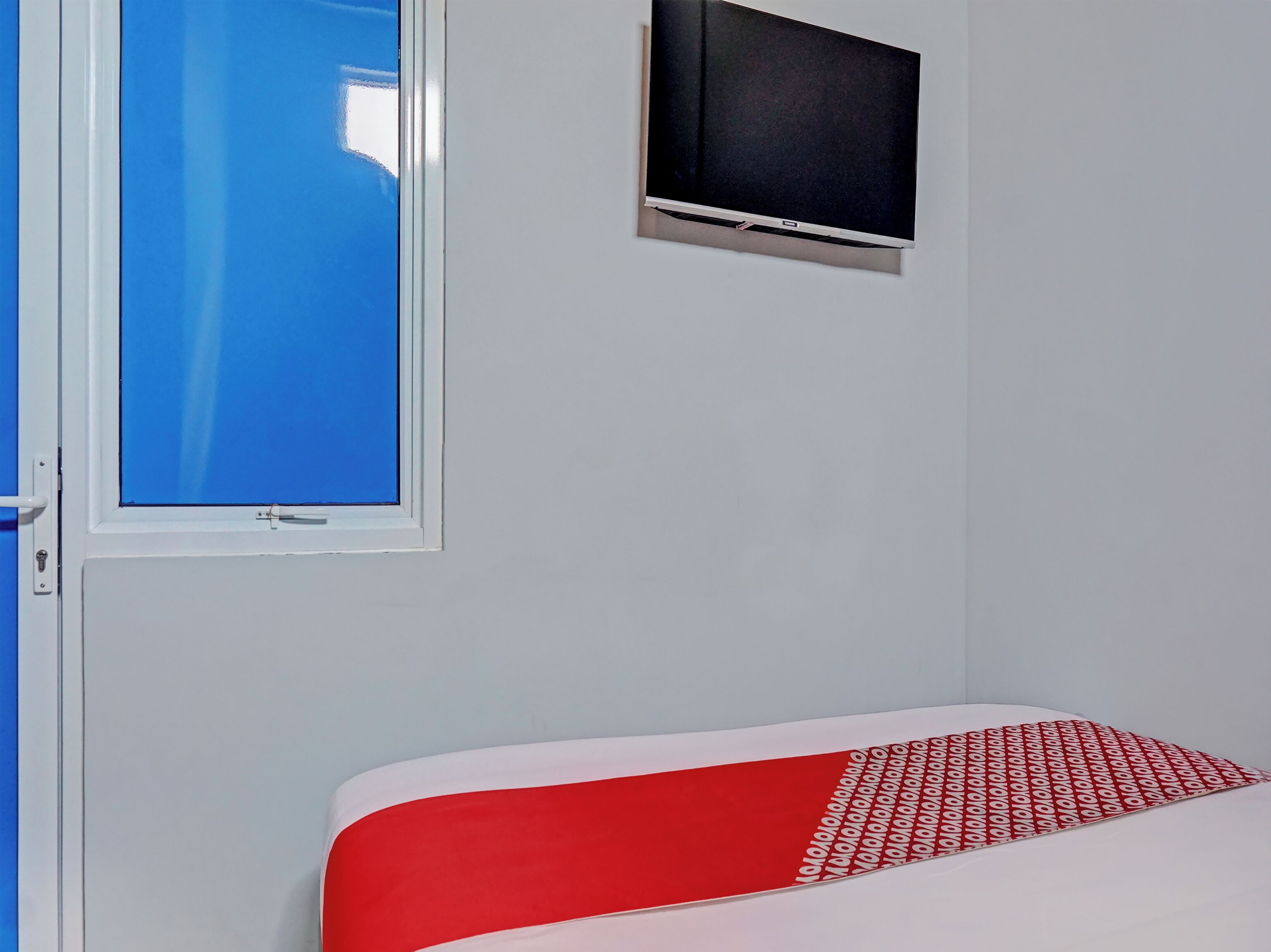 Una habitación con una cama, una ventana y un televisor montado en la pared.