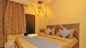 A double bed with a wooden headboard, a bedside table with a plant, and a curtain with a floral pattern. - Roomshala 103 Good Luck House (New Delhi)
