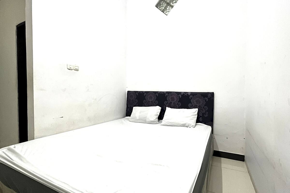 A small, single-bed room with a plain headboard and white bedding.
