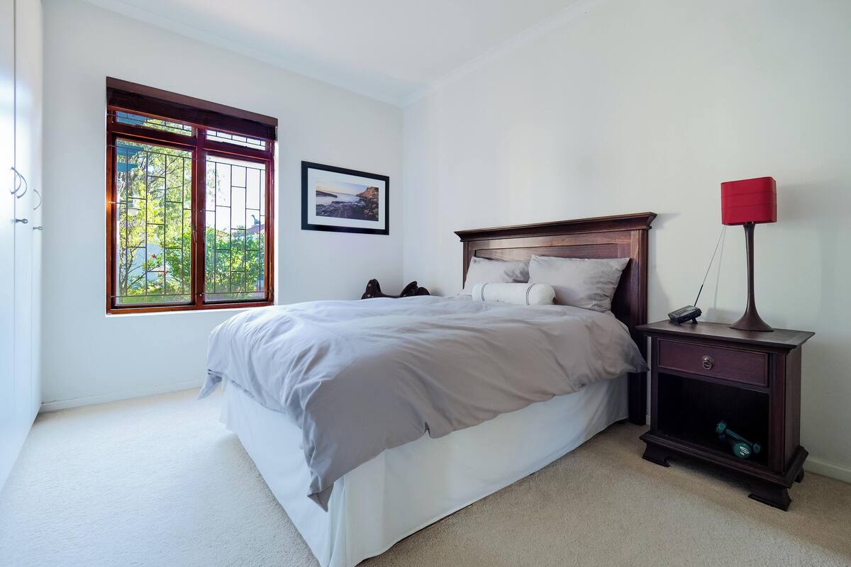 Une chambre à coucher comprenant un lit, une table de chevet, une lampe, une fenêtre donnant sur un paysage agréable et un tableau encadré accroché au mur.
