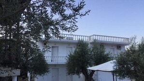 Un bâtiment blanc doté d’un balcon, d’un sol en pierre, de sièges extérieurs et de plantes en pot.