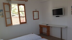 Une chambre à coucher avec un lit, un bureau, une télévision et une fenêtre avec des rideaux.