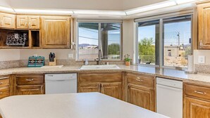 A kitchen with wooden cabinets, a granite countertop, a dishwasher, and large windows offering a view of the outdoors. - Havasu Paso - Pool, Spa, Games, Mountain Views (Lake Havasu City)