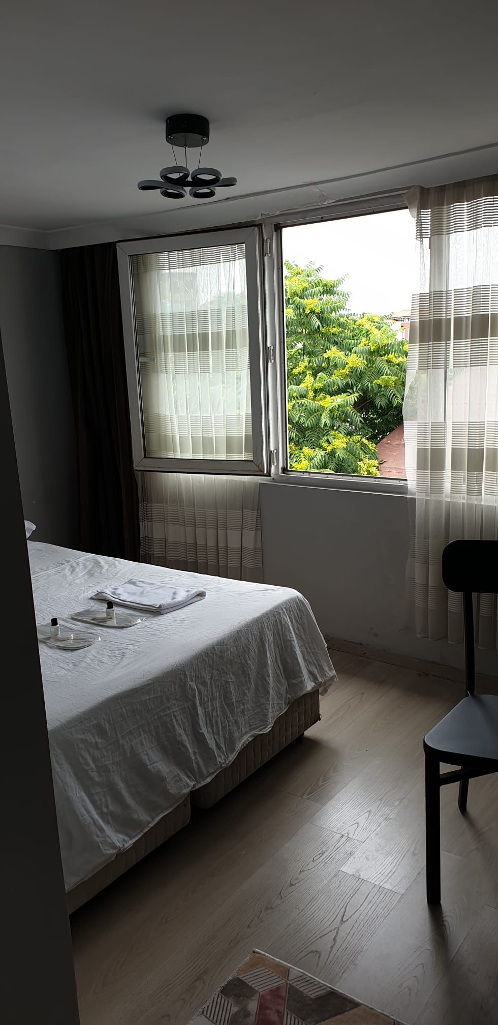 Un dormitorio con cama, una silla, ventana con cortinas y ventilador de techo.