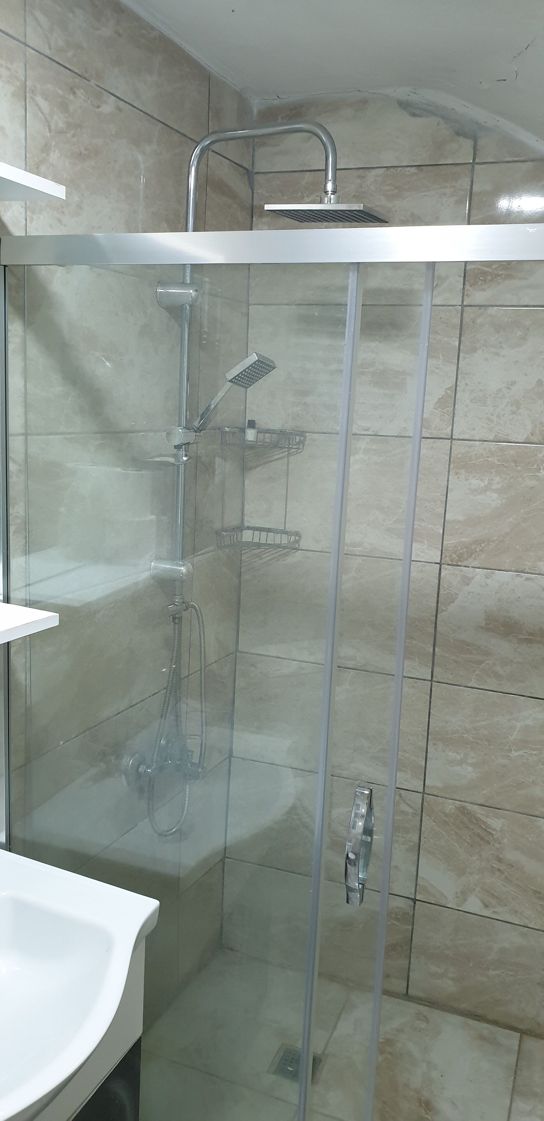 A glass-enclosed shower with a handheld showerhead and a wall-mounted faucet.