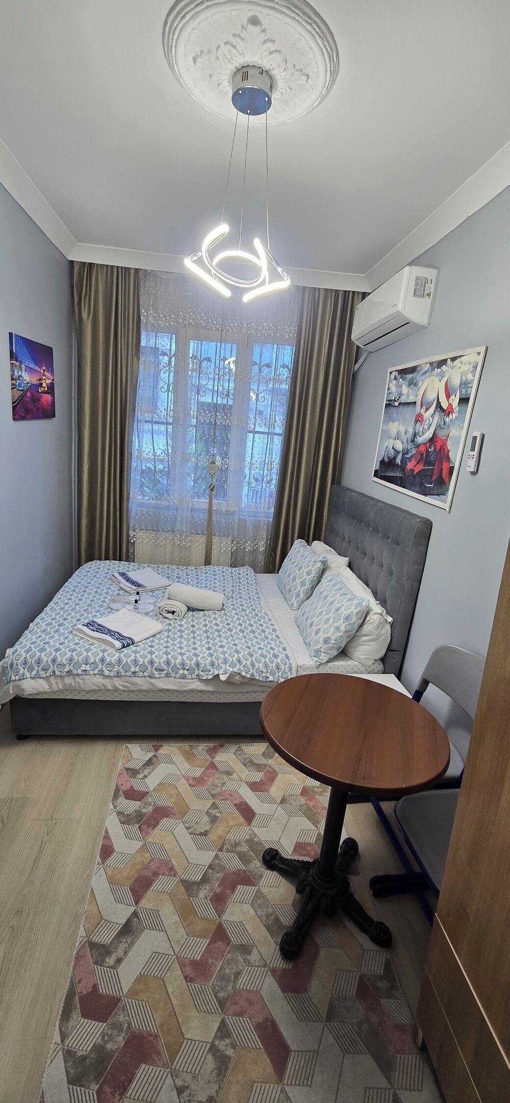 Ein Schlafzimmer mit einem Bett, einem runden Tisch, einem gemusterten Teppich und einer Deckenleuchte.