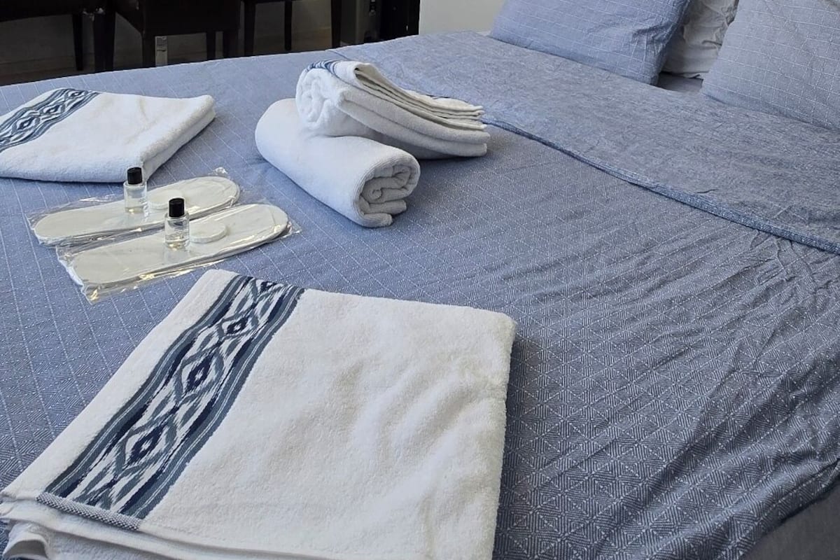Ein Hotelzimmer mit einem ordentlich bezogenen Bett, einem an der Wand montierten Flachbildfernseher, einem Schreibtisch mit Stuhl und einer modernen Deckenleuchte.