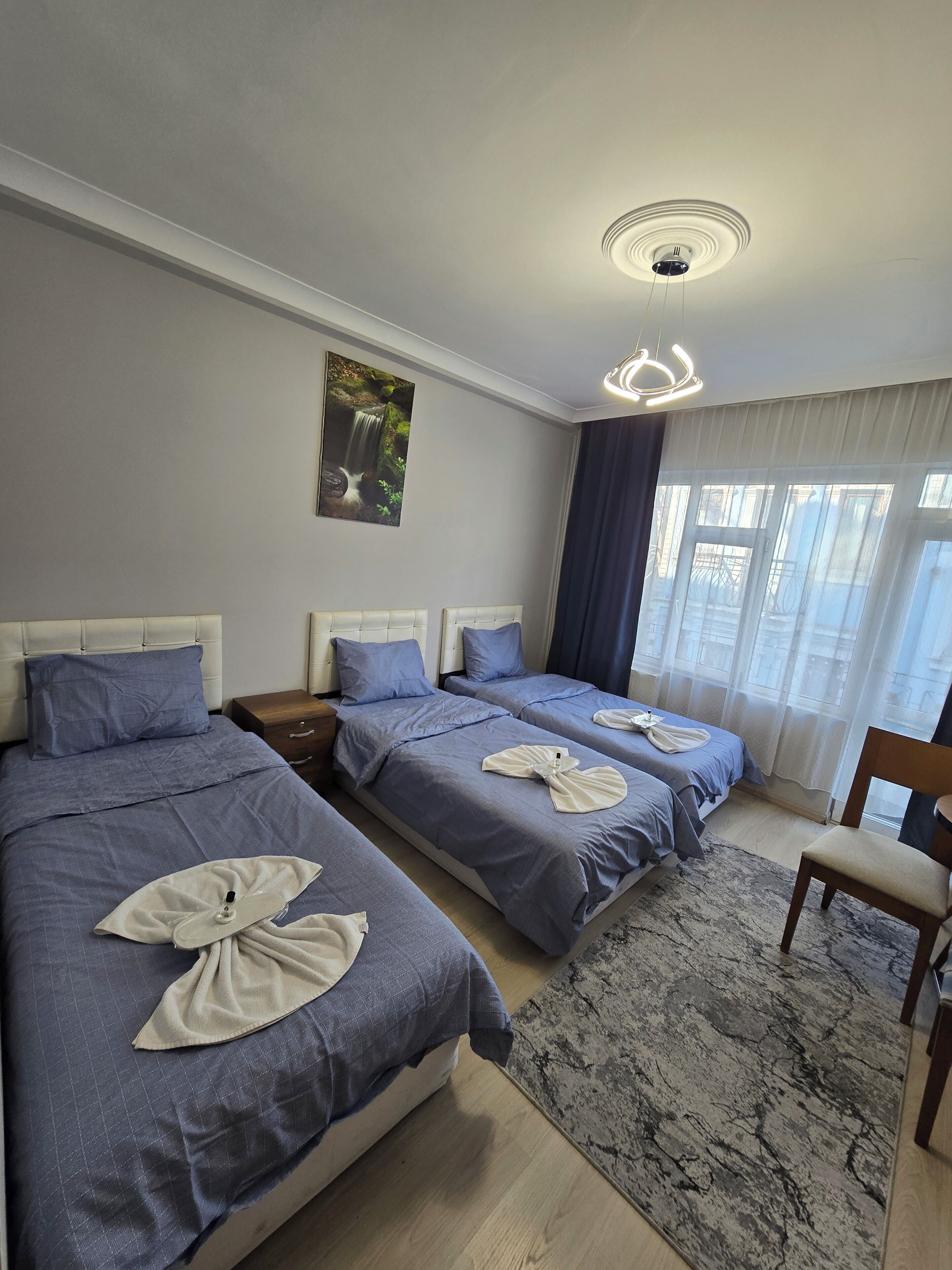 A hotel room with two beds, a wooden chair, a rug, a painting, and a ceiling light.