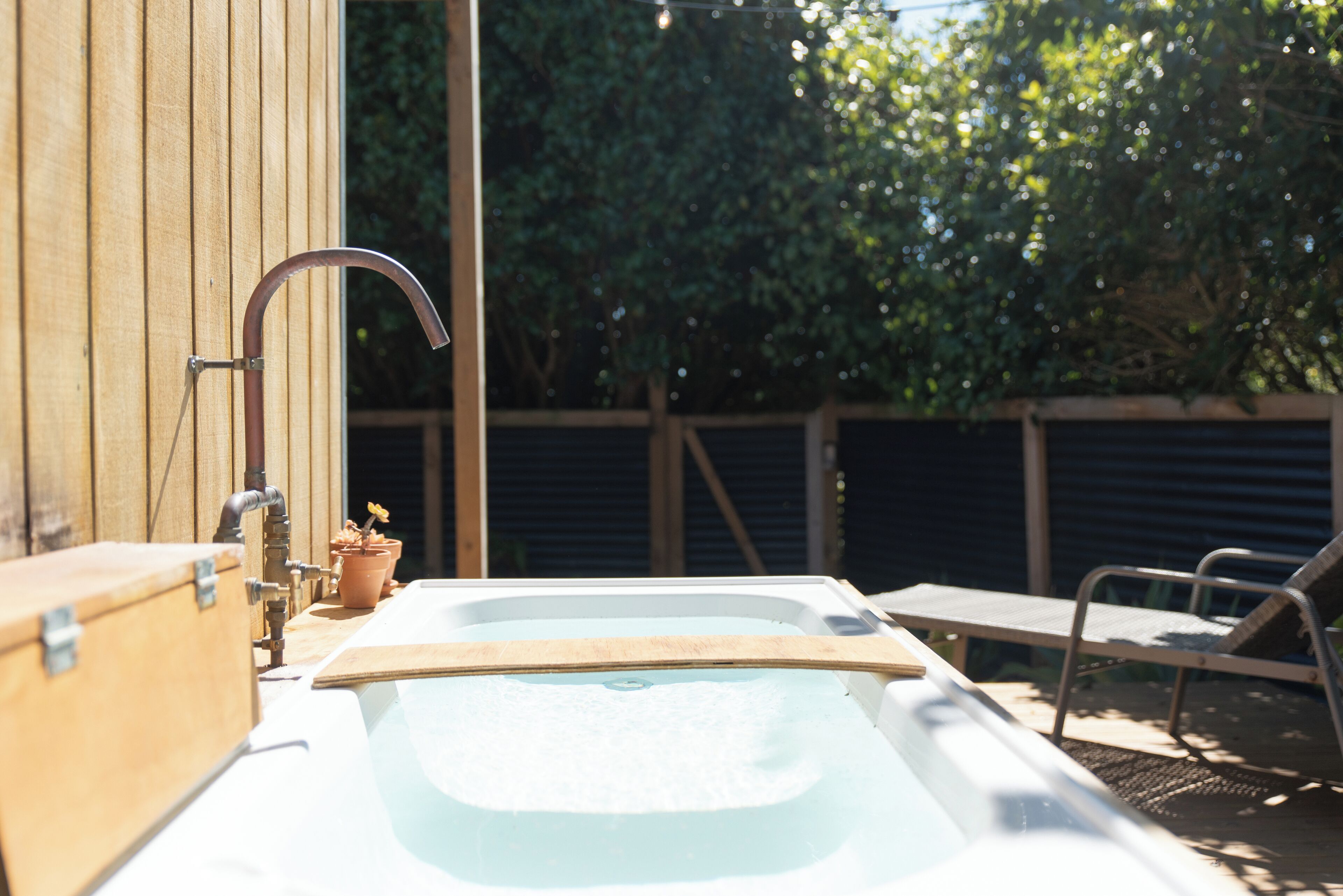 Een hottub met een houten terras, een metalen kraan en een potplant.