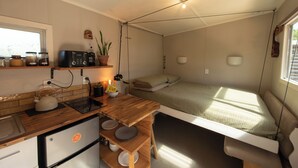 A compact, well-lit room with a kitchenette, a bed with a view, and a small dining area. - The Secret Studio, Outdoor Bath & Pizza Oven (New Plymouth)