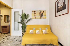 A room with a yellow bed, a framed painting, a potted plant, and a wooden cabinet.