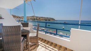 Un balcón con mobiliario de mimbre, vista al mar y una colina distante.