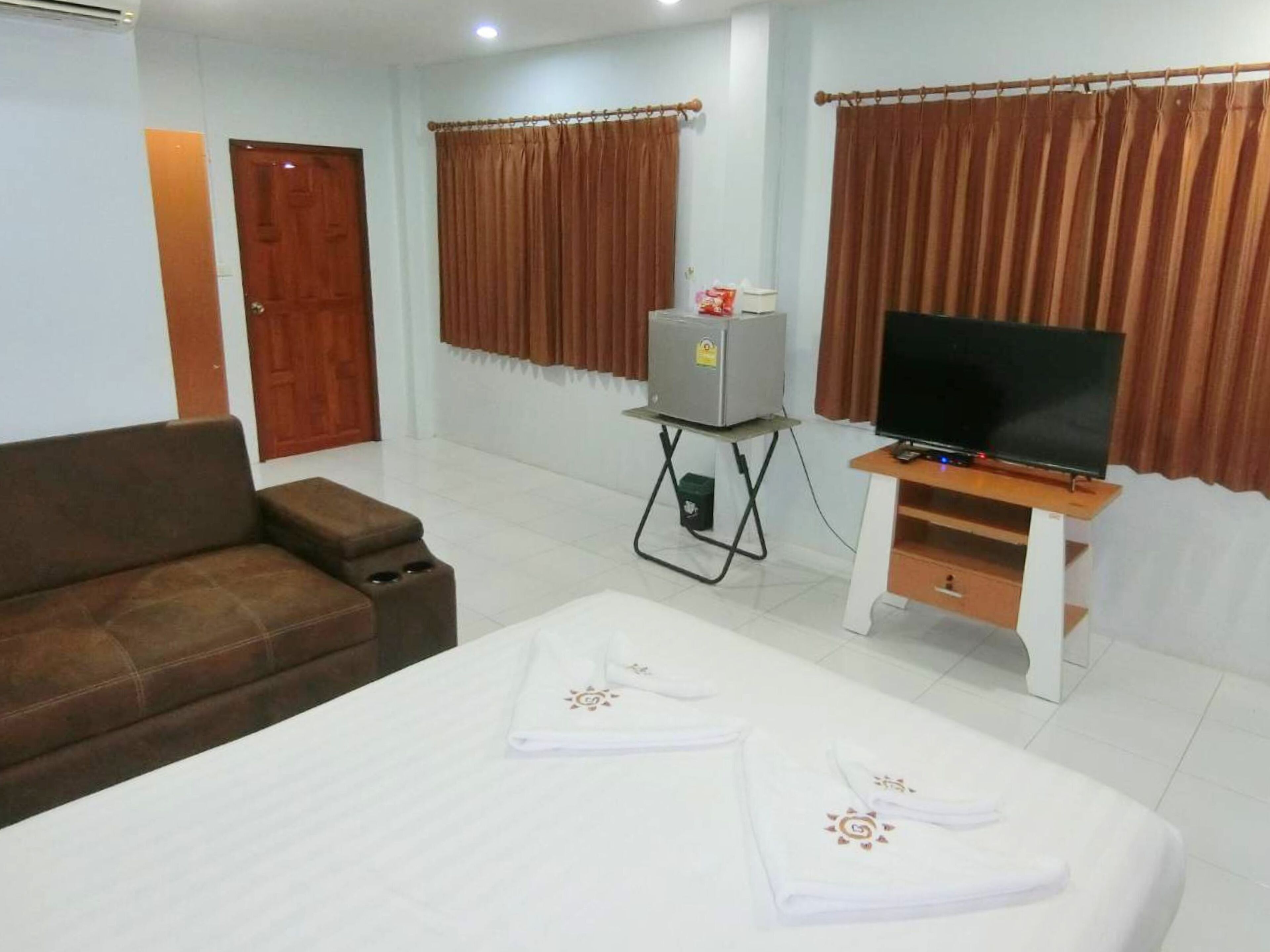 A hotel room with a bed, a sofa, a television, and a small table with a heater.