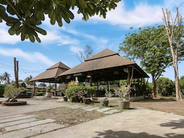A covered outdoor area with two small structures, surrounded by potted plants and trees.