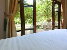 A room with a large window, a bed, and a view of a park with a bench and a lamp post.