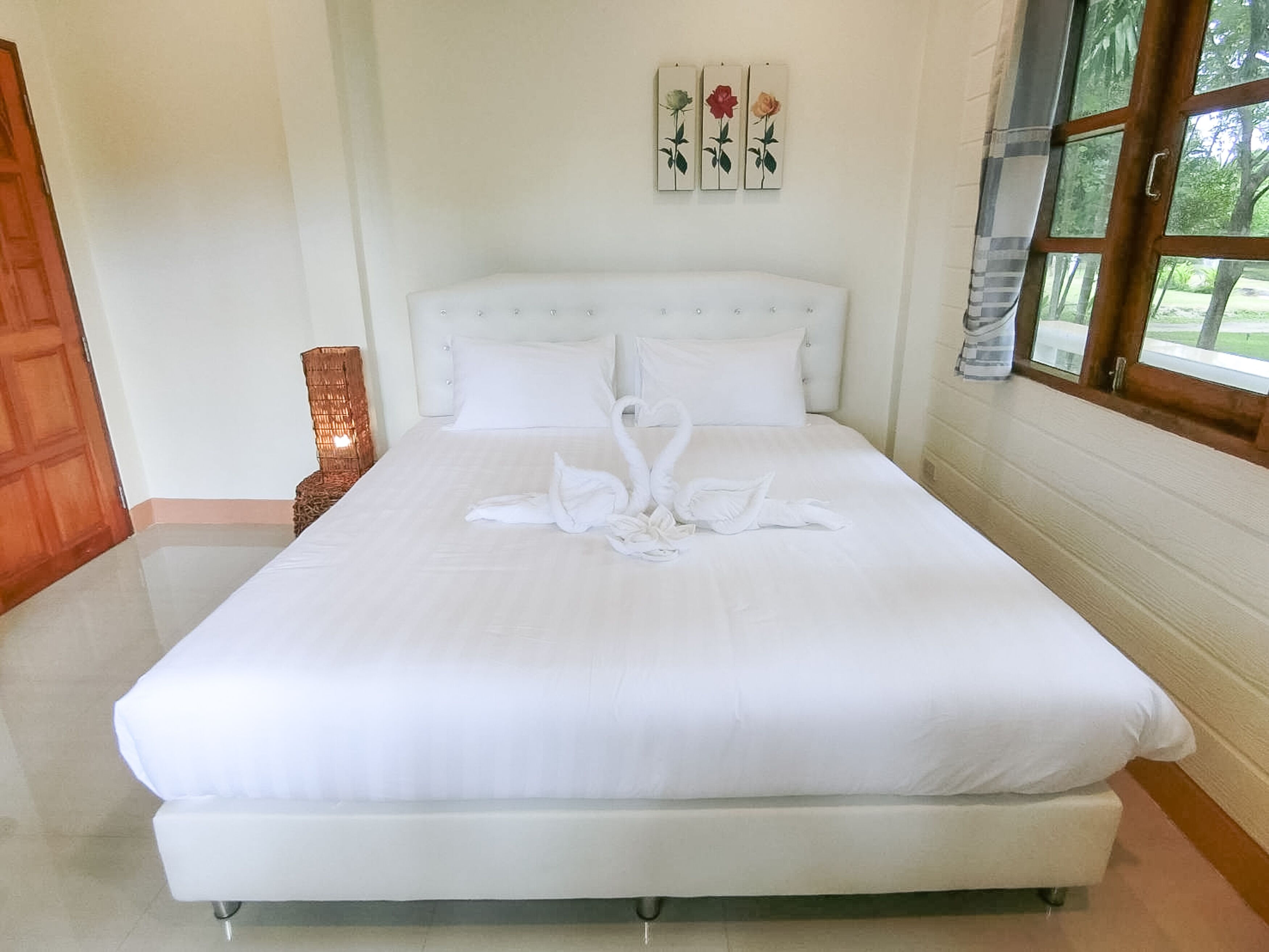 A neatly made bed with white linens and a swan-shaped towel arrangement.