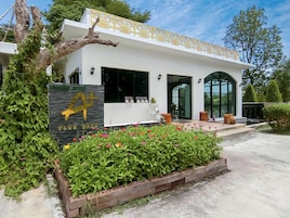 A modern building with a white facade, a large entrance, and a well-maintained garden with colorful flowers.