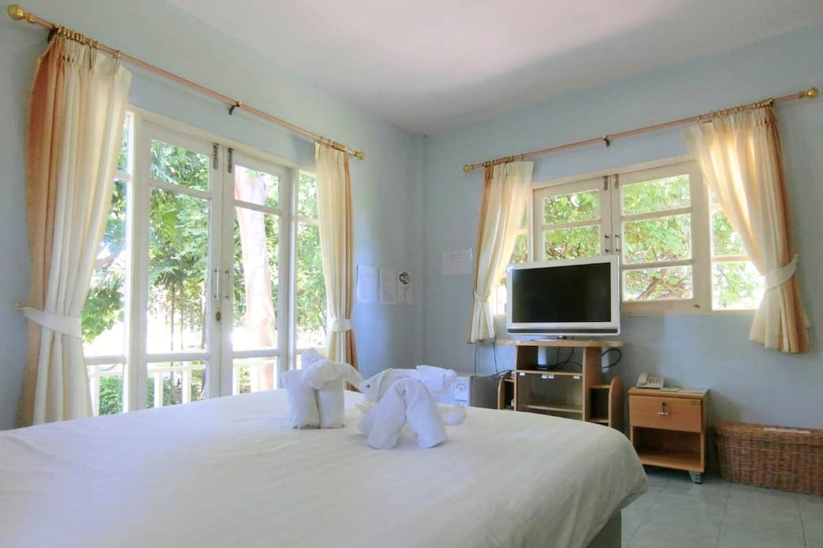 Ein Hotelzimmer mit einem großen Bett, einem Fernseher auf einem Holztisch und einem Fenster mit Vorhängen.