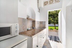 Une cuisine équipée d’un four à micro-ondes, d’un évier et offrant une vue sur un paysage verdoyant grâce à une porte ouverte.