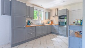 Een moderne keuken met grijze kastjes, een magnetron, oven en een raam dat voor daglicht zorgt.