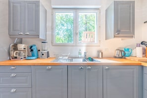A kitchen with grey cabinets, a window with a view of trees, a sink, and various appliances.