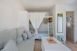 Un espace de vie compact comprenant un canapé, une petite table avec une plante, un lit superposé avec un auvent et un miroir à cadre vert.