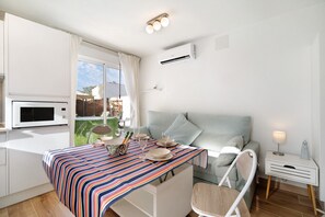 Ein modernes Zimmer mit Esstisch für vier Personen, einer Couch, einem Sessel, einer Klimaanlage und einem kleinen Nachttisch mit Lampe.