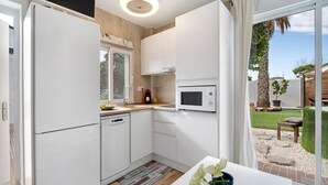 A modern kitchen with white cabinets, a built-in microwave, and a view of a garden through a glass door.
