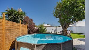 A swimming pool with a wooden fence, a tree, and a white building in the background.