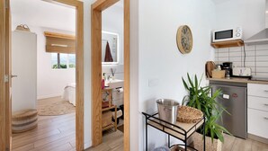 Eine moderne Küche mit Mikrowelle, Toaster und einem Edelstahlkühlschrank. Eine Holztür führt zu einem Badezimmer mit Handtuchhalter und einem Fenster.