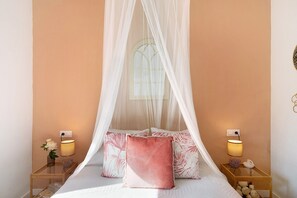 A bedroom with a canopy bed, bedside lamps, and a nightstand with a vase of flowers.