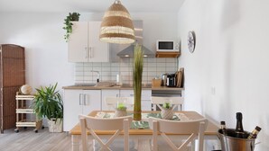 Ett modernt kök med vita skåp, en hängande lampa och ett matbord med stolar.