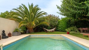 Ein Pool mit einer Fliesenleiste, umgeben von Grünflächen, einer Hängematte und einer Buddha-Statue.
