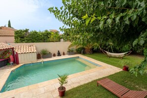 A swimming pool with a tiled deck, surrounded by grass and potted plants.
