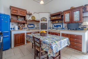 A kitchen with wooden cabinets, a blue refrigerator, a tiled backsplash, and a table with a colorful tablecloth.
